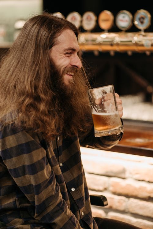 Free Bearded man with a beer mug at a pub, smiling and enjoying his drink. Stock Photo
