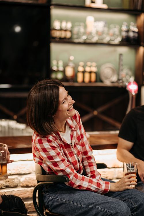 Free Woman in plaid shirt enjoying drinks and laughter at a cozy bar setting. Stock Photo