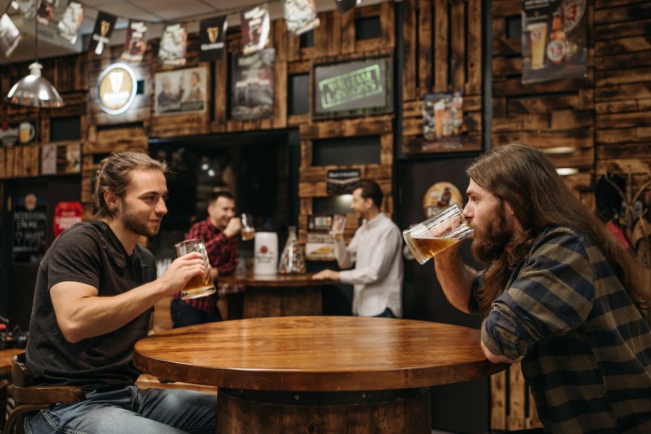 Two friends at a rustic bar savoring beers, embodying leisure and camaraderie.