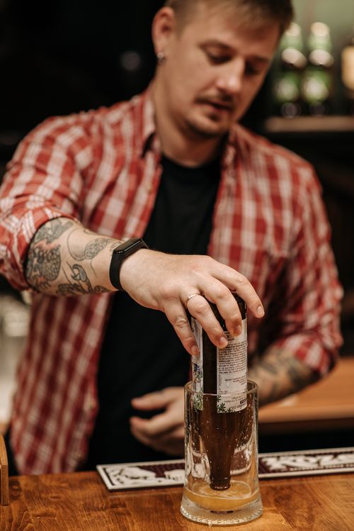 Free Bartender with tattoos mixing a beer cocktail in a cozy bar setting. Stock Photo
