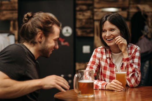 Two friends sharing laughs and drinks at a cozy indoor setting.