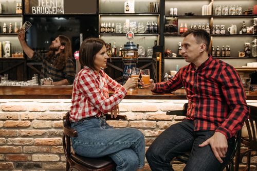 Free Friends enjoying drinks and conversation in a cozy bar setting, wearing checkered shirts. Stock Photo
