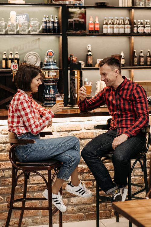 Free Friends enjoying a casual drink at a cozy bar, smiling and toasting with beer glasses. Stock Photo