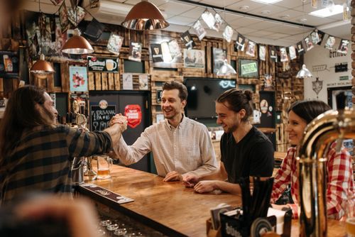 Free Group of friends enjoying arm wrestling and laughter in a cozy bar setting. Stock Photo