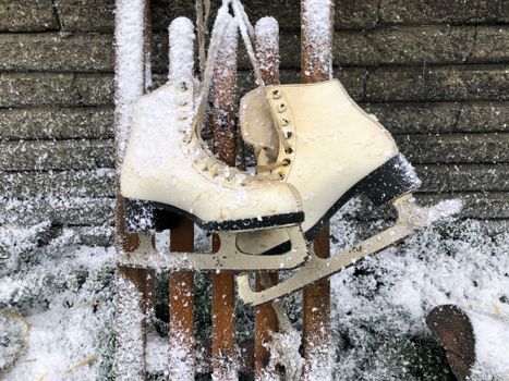 Close-up of vintage ice skates resting on a wooden sled with snowflakes creating a winter ambiance.