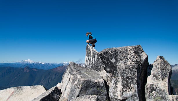 Man enjoying a thrilling moment at the peak of a majestic mountain under a clear blue sky.