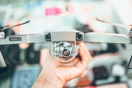 Crop unrecognizable person holding modern drone in hand and demonstrating camera against blurred interior background