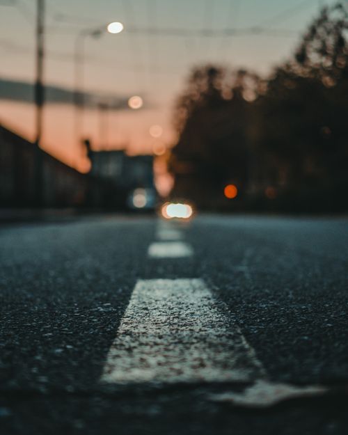 Free Low-angle view of a road in Milan with headlights blurred against a sunset backdrop. Stock Photo