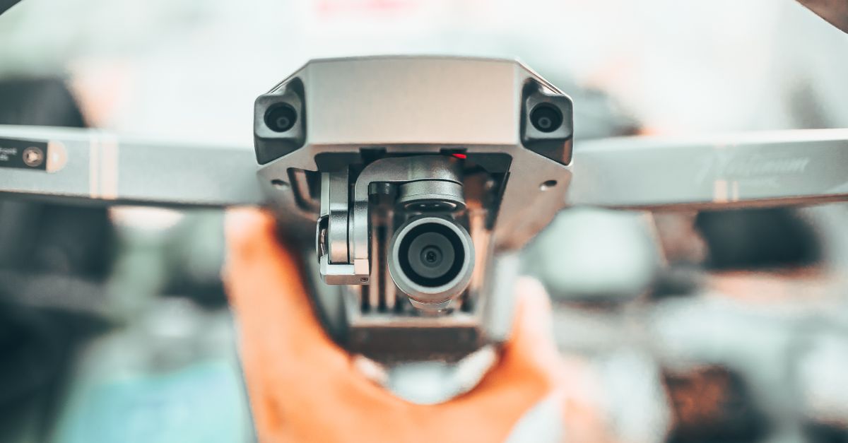 Crop unrecognizable person holding contemporary drone against blurred interior and demonstrating powerful camera