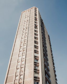 Low angle shot of a skyscraper in Milan with a clear blue sky backdrop, showcasing urban architecture.