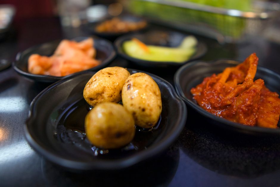 A close shot of Korean side dishes including baby potatoes and kimchi on a table.