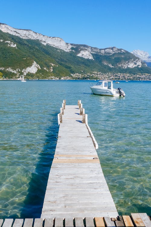 Free Rocky mountains with grass behind rippling sea with wooden pier and white yacht Stock Photo