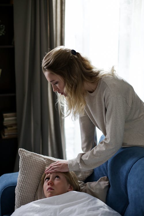 Mother Checking the Temperature of Her Daughter Lying on Sofa