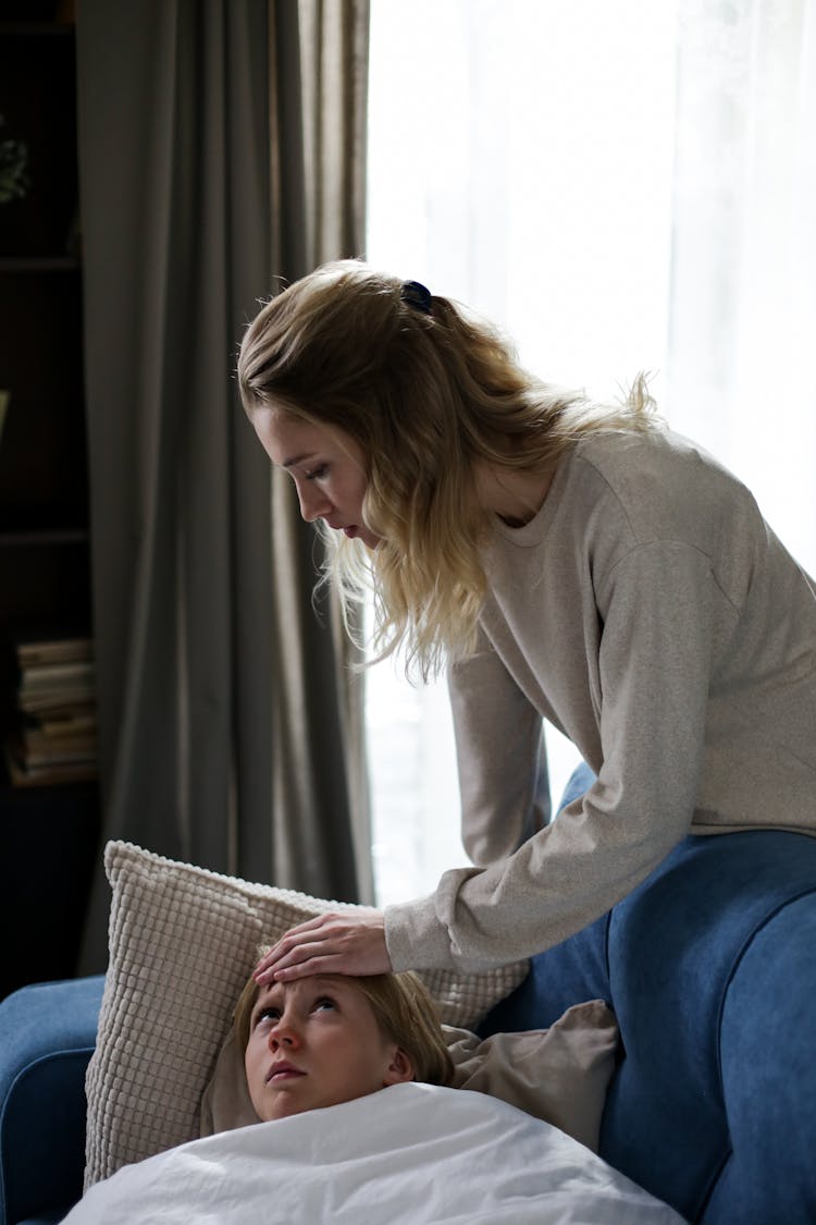 Mother Checking The Temperature Of Her Daughter Lying On Sofa