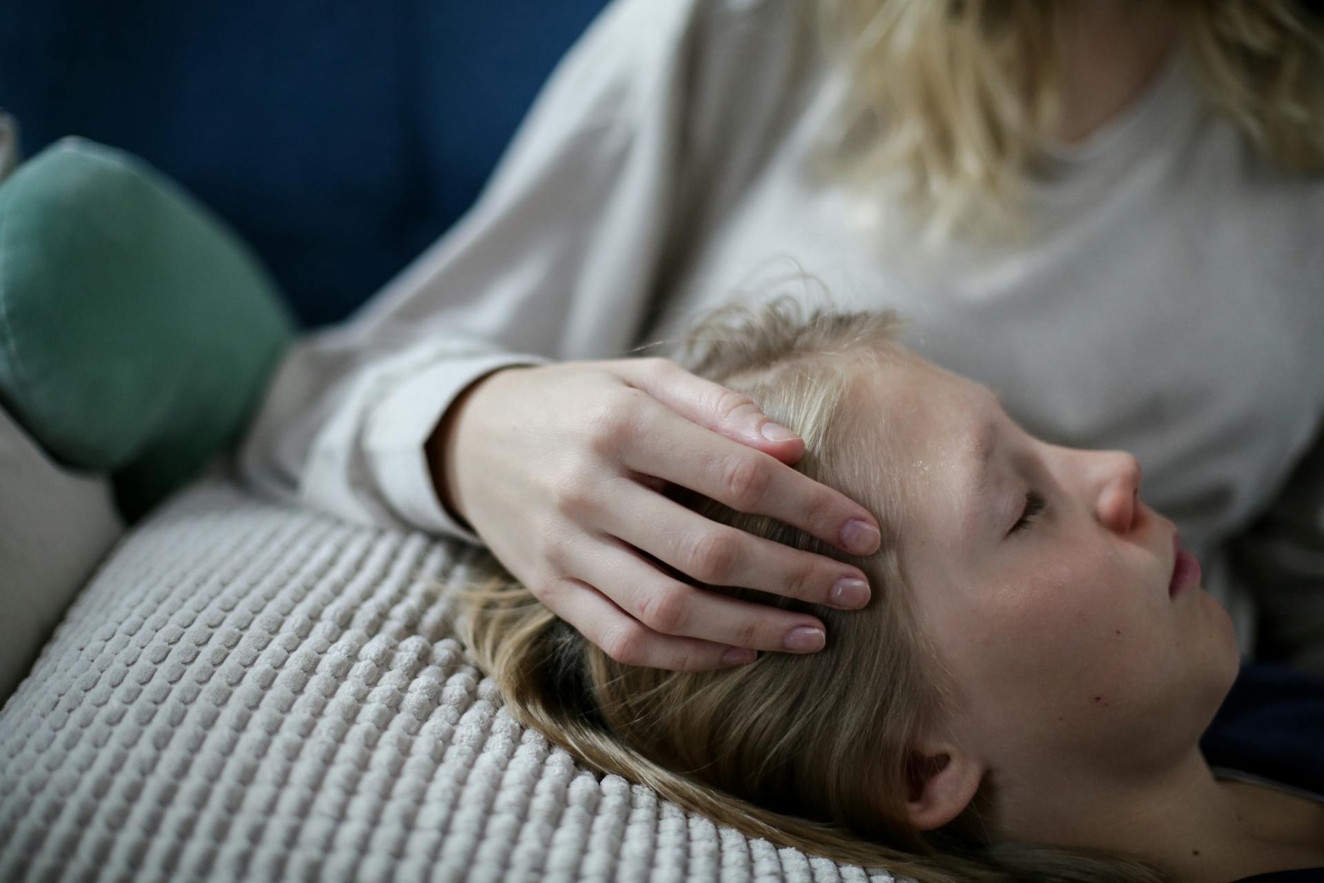 A child peacefully resting while a caregiver gently holds their head in a comforting gesture.