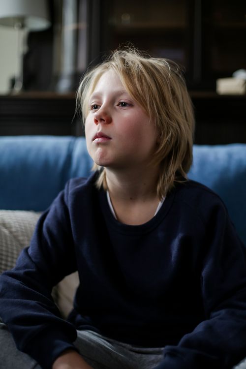 Free Thoughtful young blonde child indoors, seated on a couch, looking pensive. Stock Photo