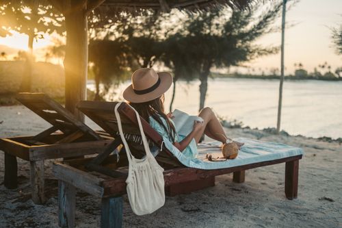 Free Woman reading on a beach lounger under a sun hat in Zanzibar at sunset, embracing vacation tranquility. Stock Photo