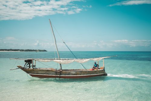 Free Two local fishermen navigate a traditional dhow on the clear waters of Zanzibar under a bright blue sky. Stock Photo