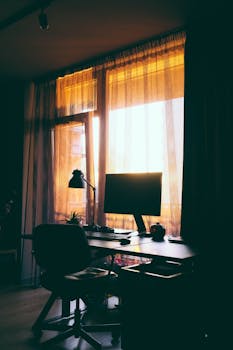 A stylish home office desk with computer monitor by a sunlit window, creating a warm work atmosphere.