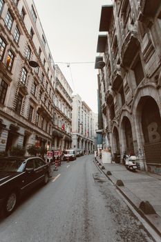 一条狭窄的街道两旁，历史建筑和停放的汽车排列在城市环境中