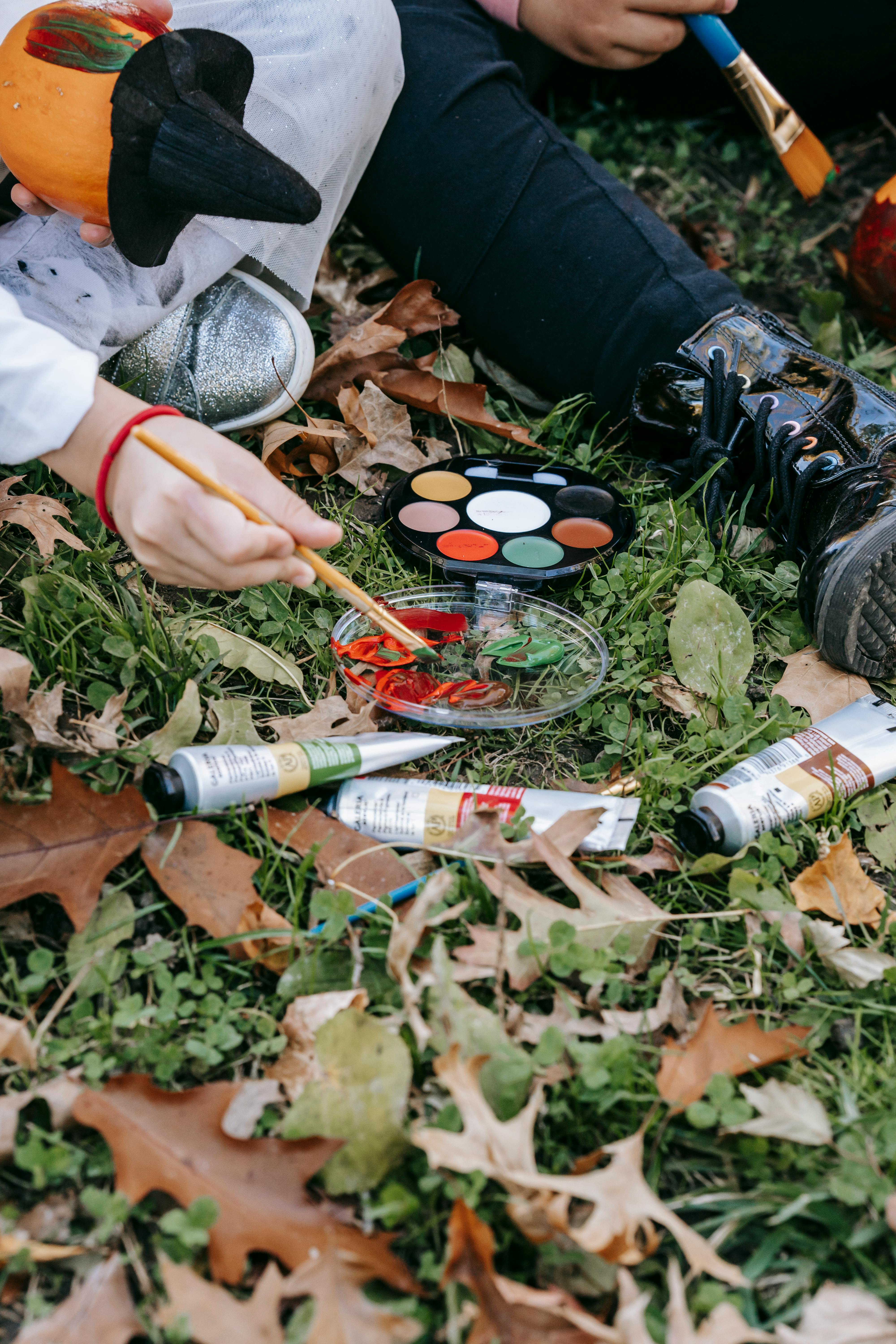 crop kids painting on pumpkins in garden