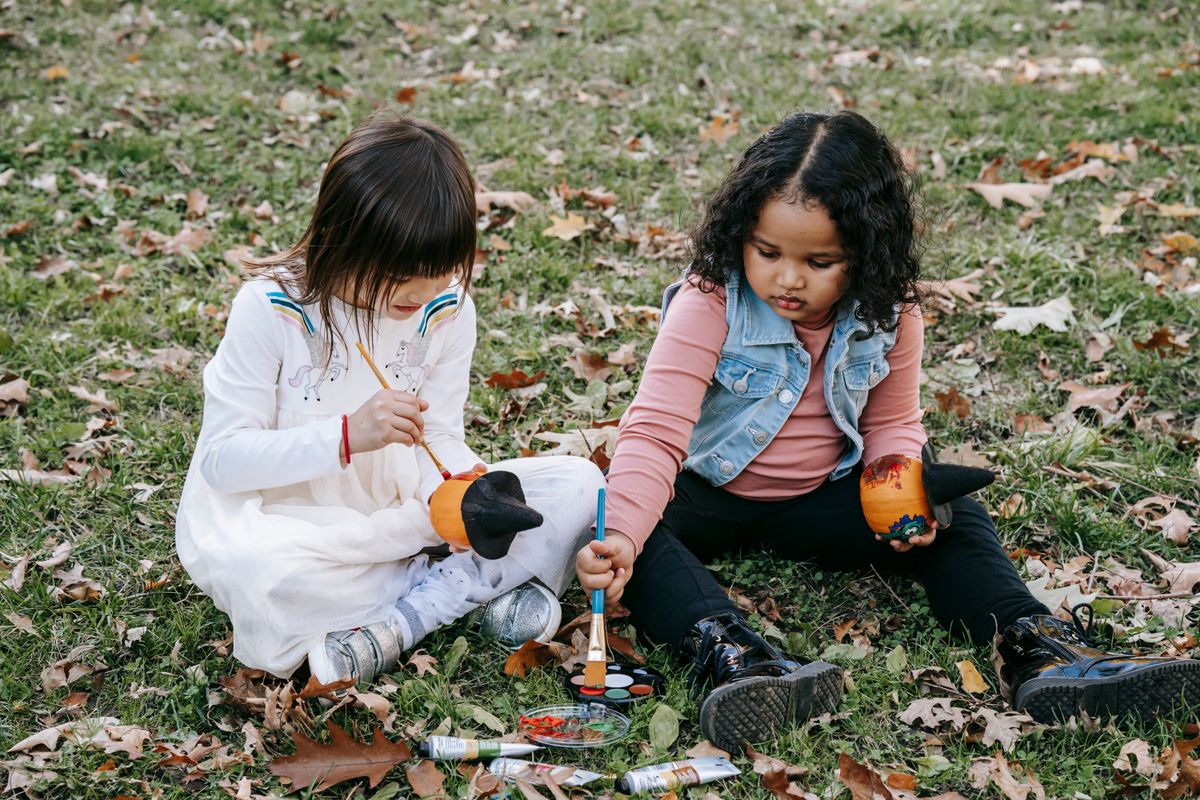 Little girls painting pumpkins together on the grass at my pumpkin painting station
