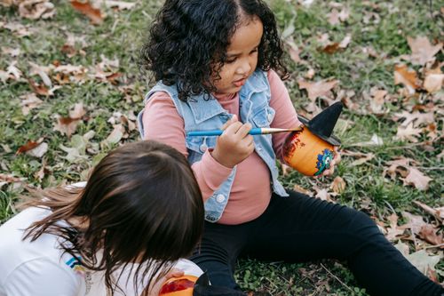 Free From above of adorable little girls in casual outfits sitting on ground and painting on small pumpkins for Halloween with brushes Stock Photo