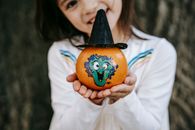 小女孩穿着白色连衣裙，展示了她为万圣节画的五颜六色的南瓜，并用纸帽子装饰着它们