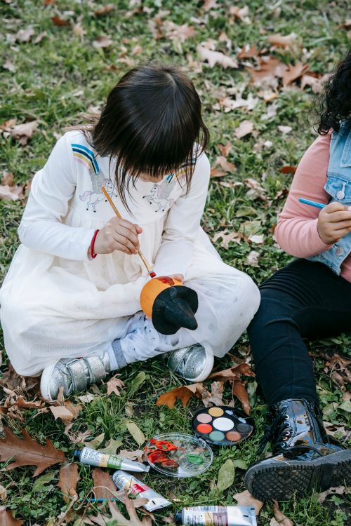 Free Unrecognizable little children in casual clothes sitting on ground in backyard and painting on pumpkins with watercolor Stock Photo