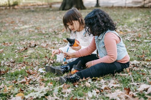 Free Full length of focused little girls painting on small pumpkins with brushes and gouache while sitting on grass Stock Photo