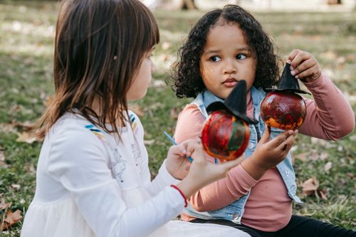 Free Adorable little girls looking at each other while sitting on ground and painting on small pumpkins Stock Photo