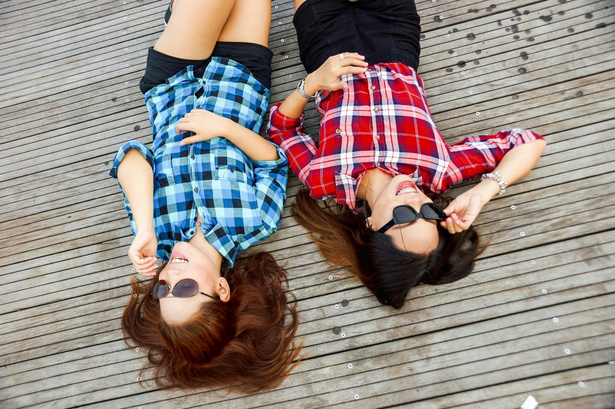 two woman wearing blue and red sport shirts and sunglasses lying on brown surface