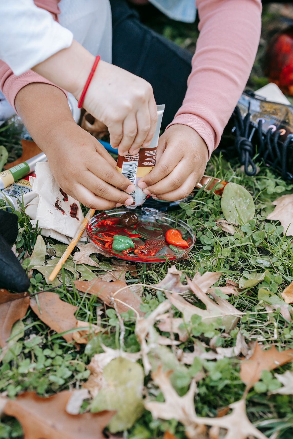 Children preparing acrylic paints for painting together on grass in a park