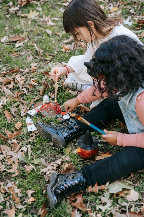 Free From above of multiethnic little friends sitting on grass and painting pumpkin with colored paints and brushes Stock Photo