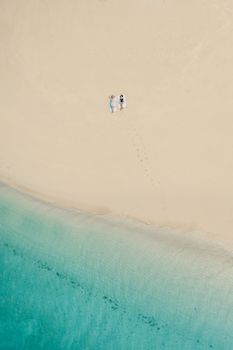 从空中俯瞰，宁静的桑给巴尔海滩上，一对夫妇正在绿松石水域边的白色沙滩上放松