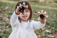 Funny girl with painted hands making scary face while playing in park during Halloween celebration