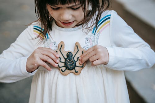 Little girl in white dress with fearful gaze with biscuit decorated with spider for Halloween