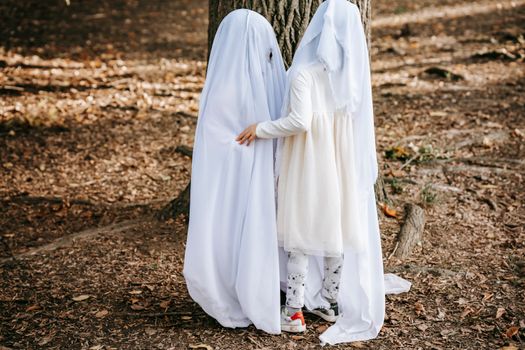 孩子们穿着幽灵服装，在秋天的公园里开心地玩耍，体现了万圣节的精神