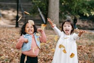 两个开朗的女孩在公园里欢快地踩着落叶，捕捉秋天的乐趣