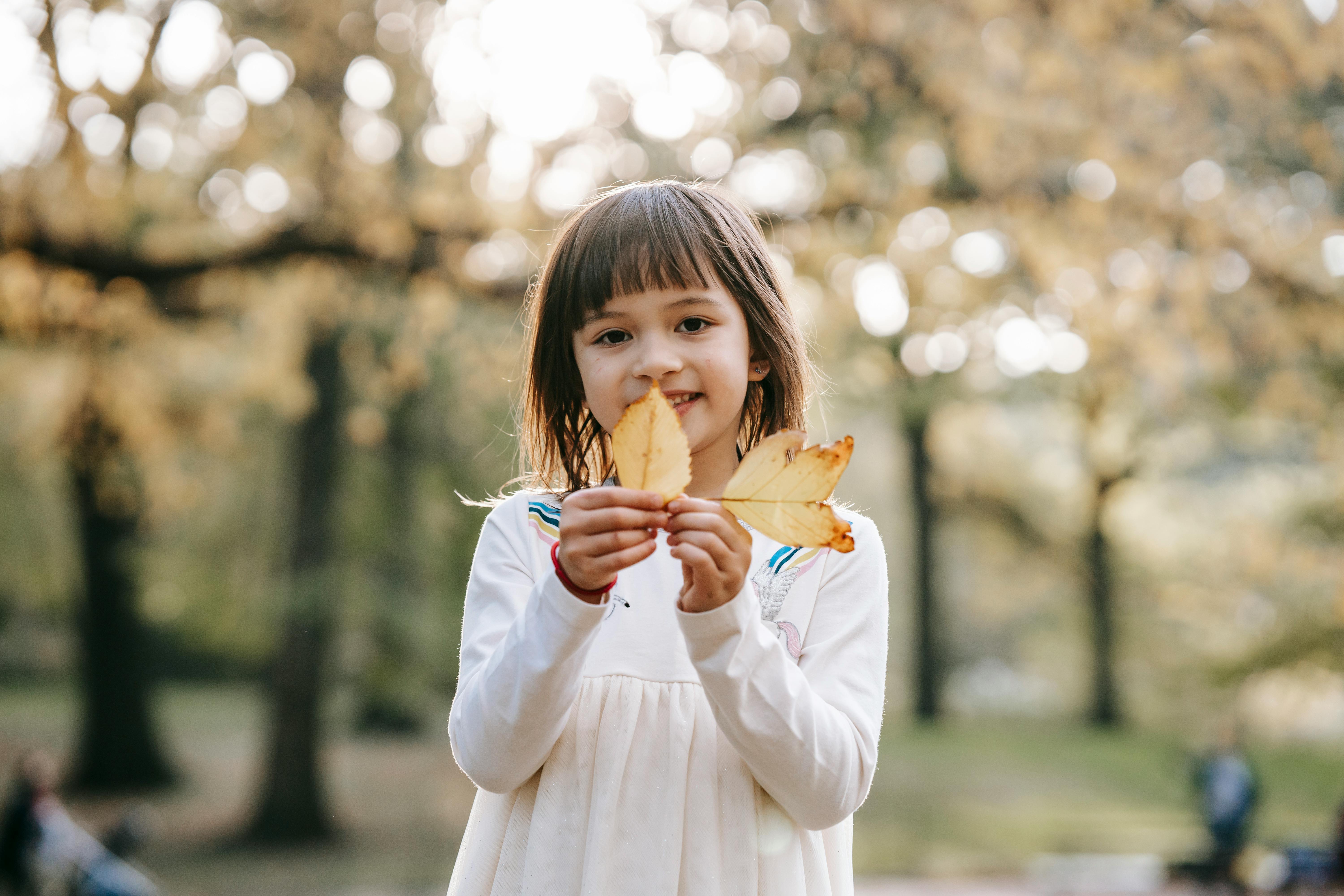 cute child demonstrating golden leaves in park