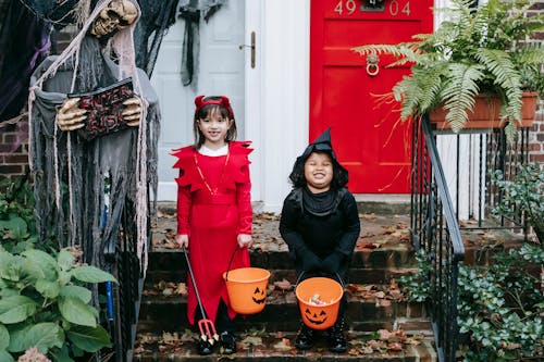 Free Full body of cheerful multiracial girlfriends in Halloween costumes holding buckets with sweets while standing on stairs together Pexels