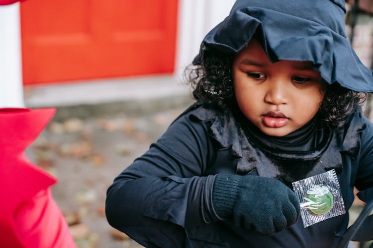 Crop Ethnic Kid With Candy In Halloween Celebration