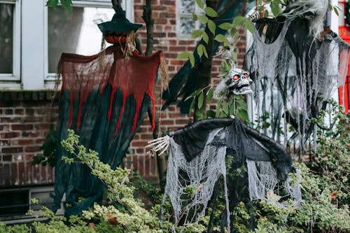 Spooky skeleton and witches on wooden sticks near entrance of brick house on Halloween