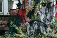 Spooky skeleton and witches on wooden sticks near entrance of brick house on Halloween