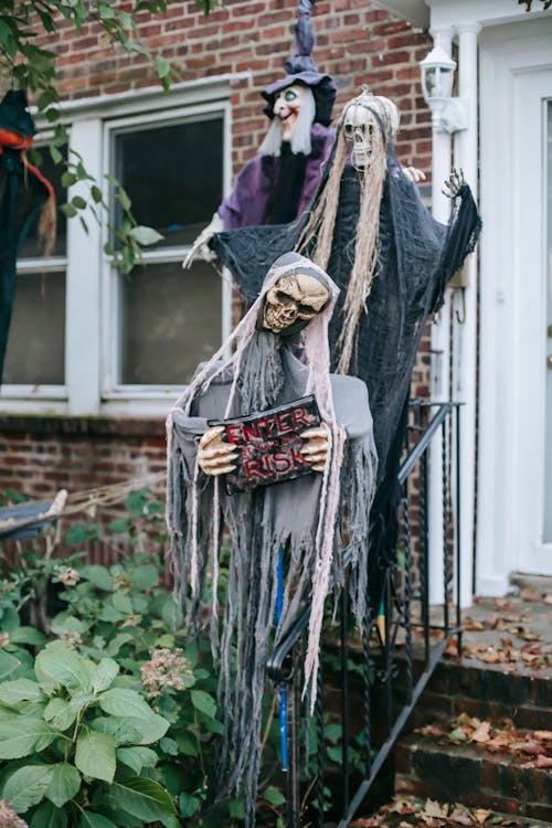 Horror scarecrows with skulls and torn apparel on fence of building on Halloween