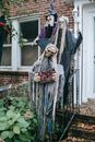 万圣节建筑的栅栏上挂着恐怖稻草人，它有头骨和撕裂的服装