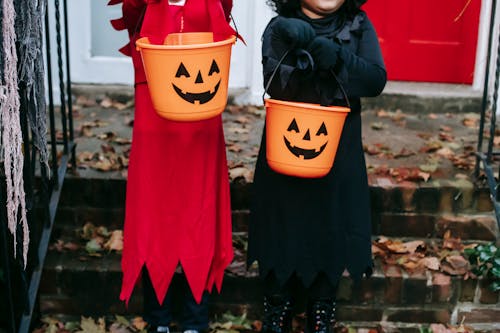 Free Crop faceless kids in spooky costumes standing on stairs and holding buckets for treats in Halloween Stock Photo