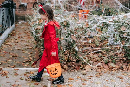 Child in devil costume on Halloween strolling with bucket