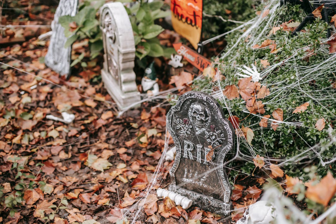 Fake graves covered in web with bones lying around near signs trick or treat and home sweet home on Halloween in autumn day