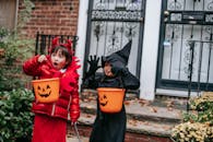 Funny children in witch and devil costumes carrying buckets for candies and showing creepy grimaces against house in neighbourhood